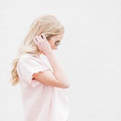 a blonde woman with sunglasses on talking on her cell phone while standing in front of a white wall