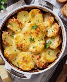 a casserole dish with potatoes and parmesan cheese on the side next to bread