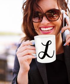 a woman is holding a coffee mug and talking on her cell phone while smiling at the camera