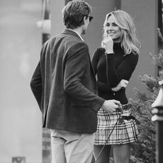 a man standing next to a woman talking on a cell phone while wearing a skirt