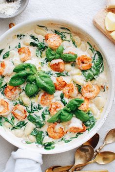 pasta with shrimp, spinach and cheese in a white bowl next to spoons