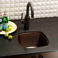 a black counter top with a sink and some green apples on the plate next to it