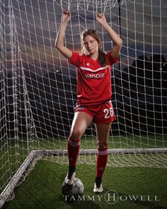 a female soccer player is posing in front of the net with her arms up and head down