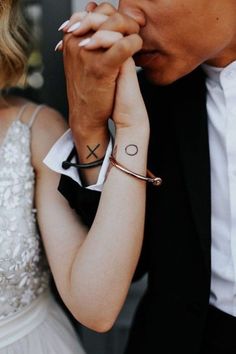 a man and woman are holding hands with tattoos on their wrists, while one holds the other's hand