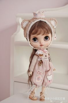 a doll with long hair and big eyes wearing a bear hat, dress and shoes