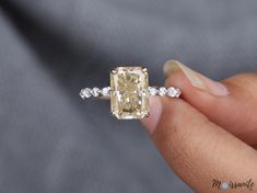 a woman's hand holding an engagement ring with a yellow diamond in the center