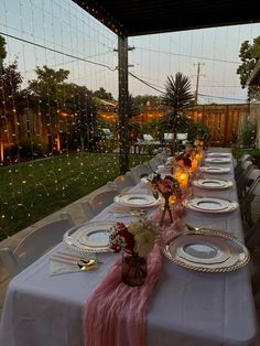 a long table is set with plates and silverware for an outdoor dinner or party