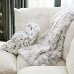 a stuffed owl is laying on the arm of a couch with a blanket over it