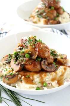 two white plates topped with mashed potatoes covered in mushrooms and green garnish