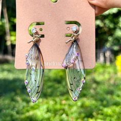 a pair of butterfly wings are hanging from the back of a pink card with green grass and trees in the background