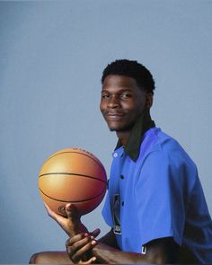 a man holding a basketball in his right hand and smiling at the camera, against a blue background