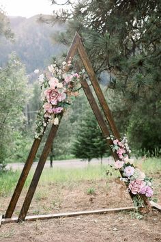 a wooden triangle decorated with flowers and greenery for a wedding ceremony in the woods