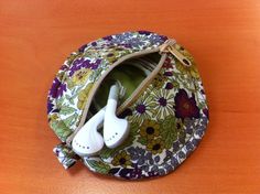 an electronic device in a floral purse on a wooden table with ear buds plugged into it