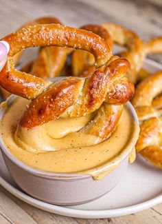 pretzels being dipped with mustard in a bowl on a plate next to other pretzels