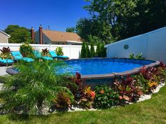 an above ground swimming pool surrounded by plants and flowers in a backyard with a fence around it