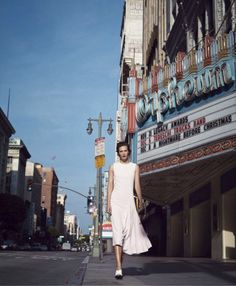 a woman walking down the street in front of a movie theater on a sunny day