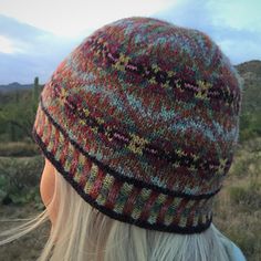 a woman with blonde hair wearing a multicolored knitted hat in the desert