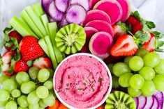 various fruits and vegetables arranged in a circle with dip on the top, including grapes, celery, strawberries, kiwis, carrots, radishes