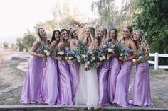 a group of women standing next to each other wearing purple dresses and holding bouquets