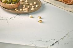 an assortment of olives and pistachio on a marble countertop with a copper bowl