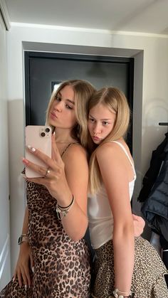 two young women taking a selfie in front of a mirror with their cell phone