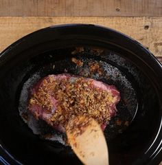 a piece of meat is being cooked in a crock pot with a wooden spoon