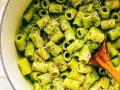 a wooden spoon in a pot filled with pasta and broccoli pesto sauce