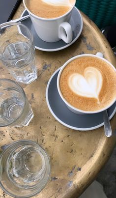 two cups of cappuccino on a table with water glasses and spoons