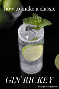 a glass filled with ice and limes on top of a black table next to green apples