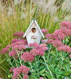 a bird house sitting on top of a bush filled with pink flowers and green leaves