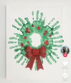 a handprinted christmas wreath is displayed on a white surface with red ribbon around it