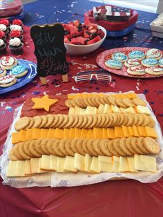 an assortment of cheese and crackers on a red table cloth with other desserts