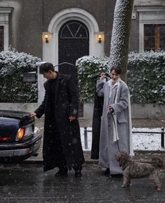 a man and woman walking their dog on a snowy day in front of a house