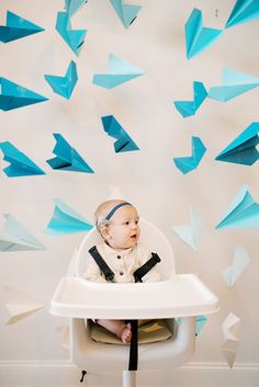 a baby is sitting in a high chair with blue paper airplanes flying above him on the wall