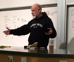 a man standing in front of a whiteboard with writing on the wall behind him