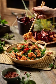 a person holding chopsticks over a bowl of food on a table with other dishes