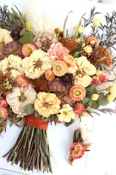 a bouquet of flowers sitting on top of a white table next to an orange vase