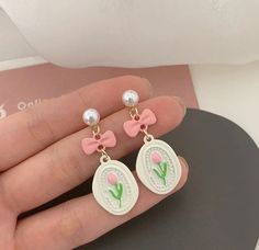 a pair of pink bowknot earrings with pearls on the bottom and an image of a