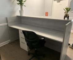 an office desk with a black chair and potted plants