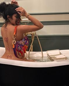 a woman with tattoos on her back sitting in a bathtub