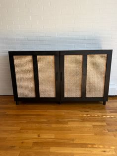 a black cabinet with wicker doors sitting on top of a hard wood floor