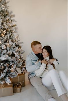 a man and woman sitting next to a christmas tree