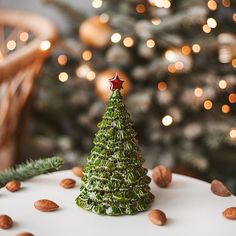 a small green christmas tree sitting on top of a white cake covered in almonds