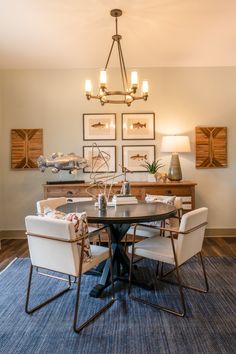 a dinning room table with chairs and pictures on the wall behind it, along with two lamps