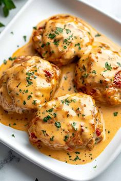 some meatballs covered in gravy and garnished with parsley on a white plate