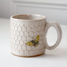 a ceramic mug with bees on it sitting on a white countertop next to a window