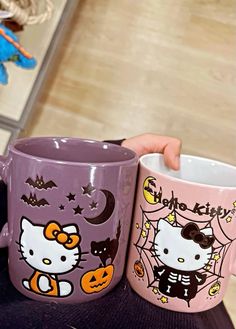 two hello kitty coffee mugs sitting on top of a table