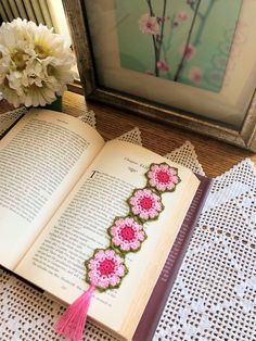 an open book sitting on top of a table next to a vase filled with flowers