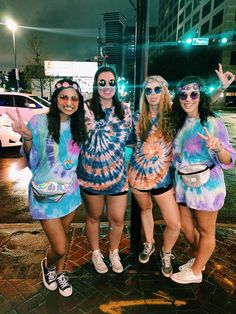 four girls dressed in tie - dyed outfits posing for the camera on a city street at night