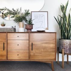 a wooden dresser sitting next to a mirror and potted plants